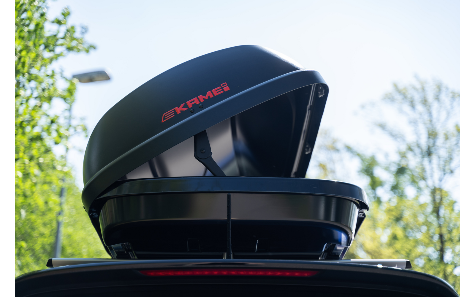 Box da tetto nero aperto sul tetto di un'auto, scritta rossa, alberi sullo sfondo