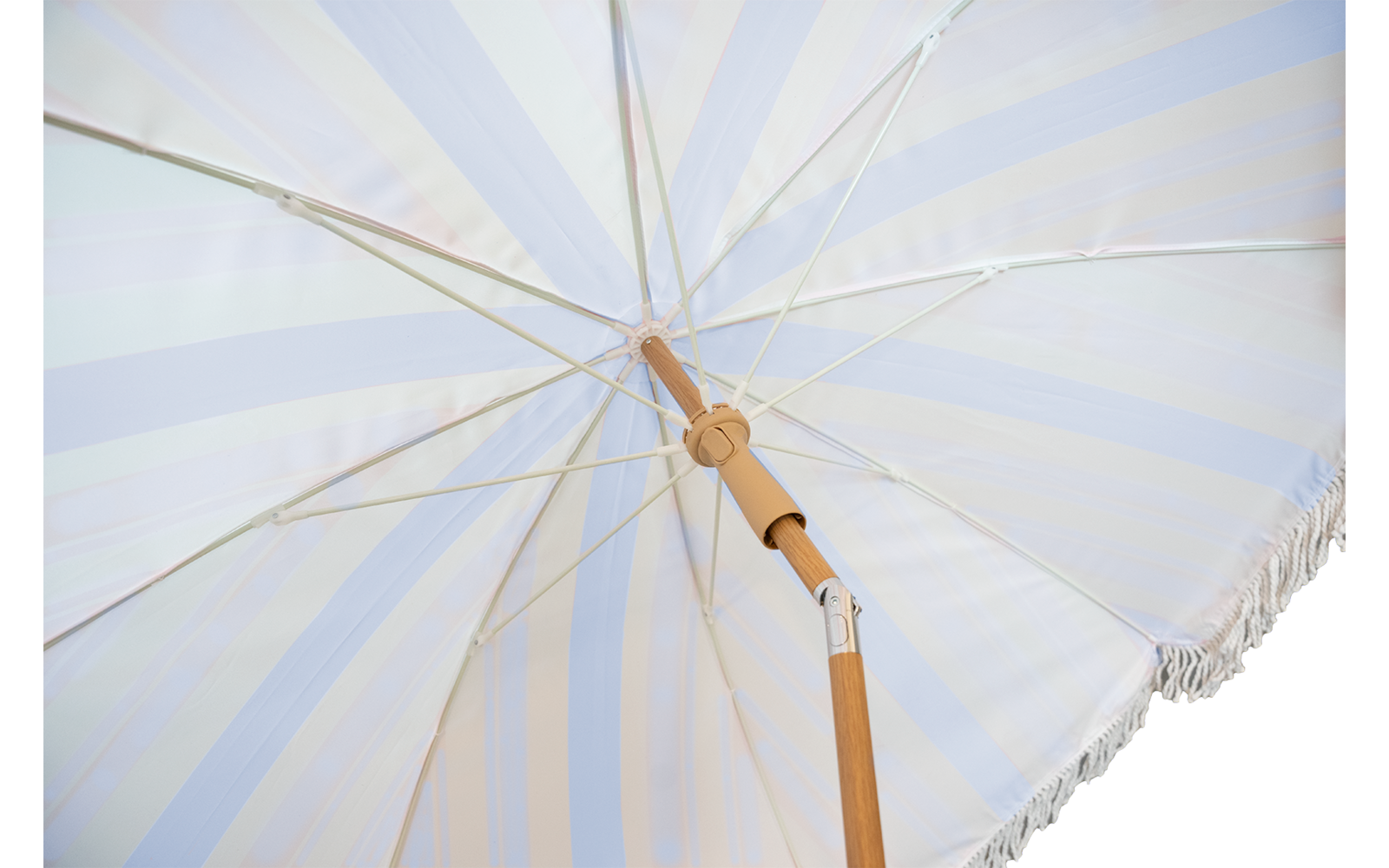 Unterseite eines aufgeklappten Sonnenschirms mit hell gestreiftem Stoff, Holzstange und Fransen am Rand