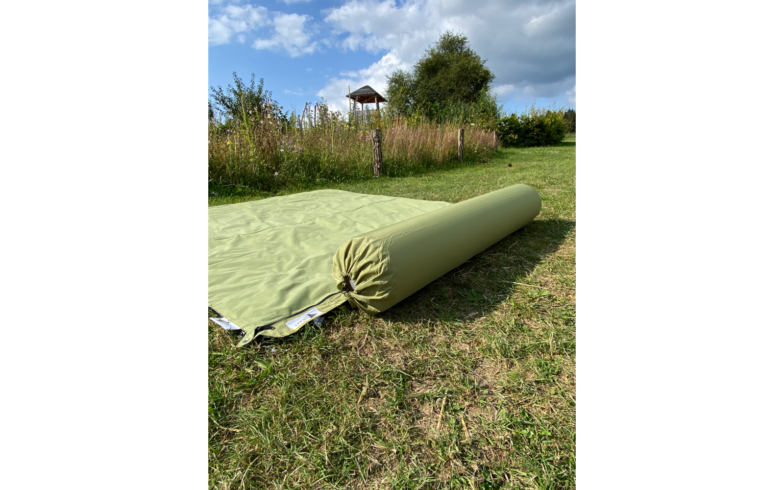 Grünliches aufgerolltes Isomatten-Innenleben liegt auf einer ausgebreiteten Isomatte auf Gras