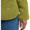 Groene teddyfleece met "Jack Wolfskin"-logo ter hoogte van de heup, rechterhand langs het lichaam, blauwe spijkerbroek