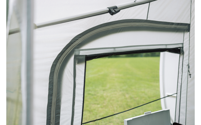 Hellgrauer Stoff mit dunkelgrauen Nähten und offenem rechteckigem Fenster, schwarzer Reißverschluss und Kordeln sichtbar, grüner Rasen im Hintergrund, weißes rechteckiges Objekt unten rechts