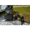 Gas stove in a black folding case with a small pot, next to a black two-step stool with a travel mug and a small potted plant on a patterned outdoor mat beside a caravan