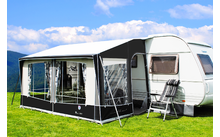 Caravan with attached awning on a green meadow under a blue sky