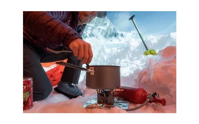 Kleiner Metallbrenner mit rundem Brennereinsatz, drei ausgeklappte silberne Topfstützen und geflochtener Metall-Gasschlauch mit Anschluss