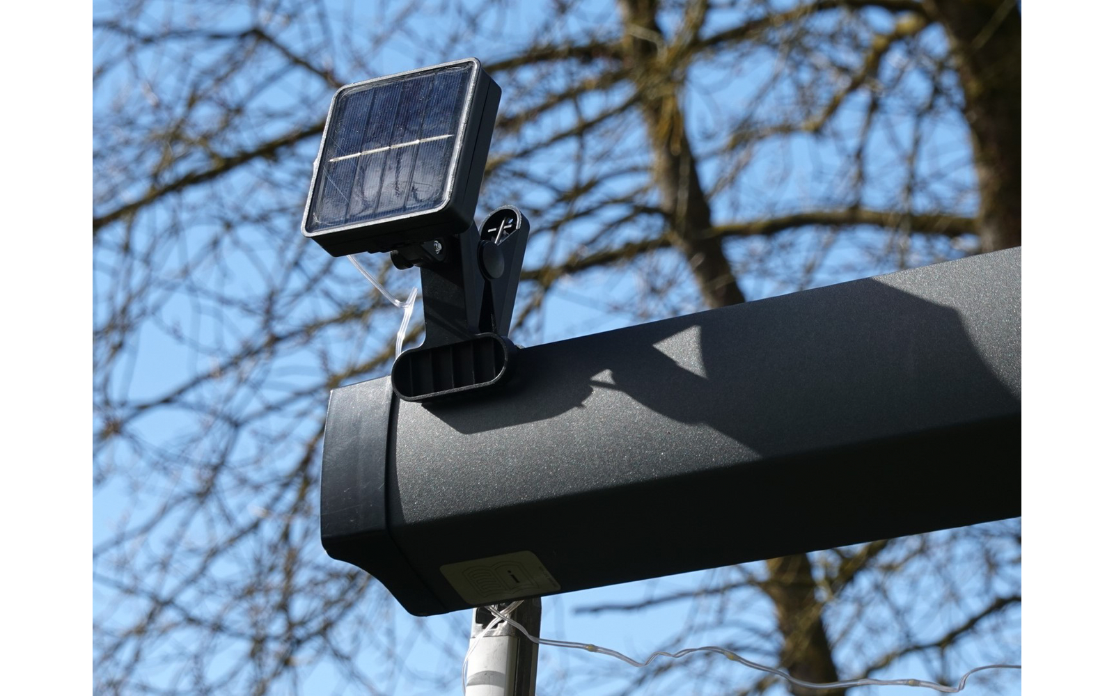 Solarlampe auf einem schwarzen Rohr mit Baumstämmen im Hintergrund