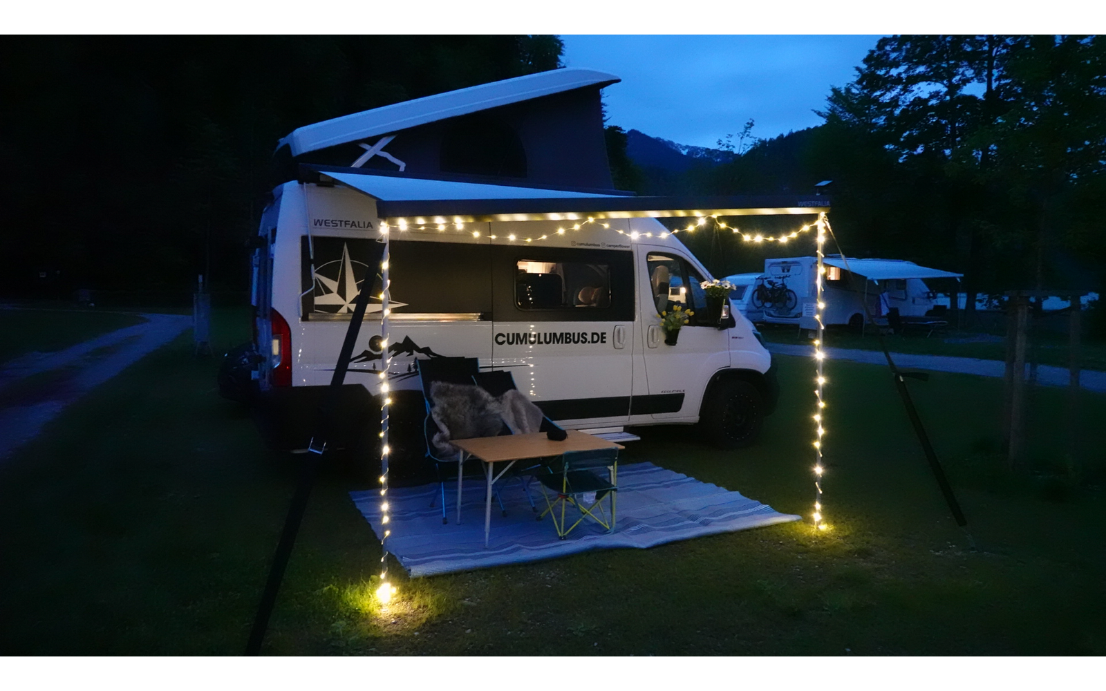 Campingwagen mit ausgeklapptem Heck und Außenbeleuchtung bei Nacht