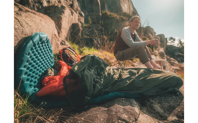Persoon ligt met rugzak op een rots, twee andere personen zitten op de achtergrond