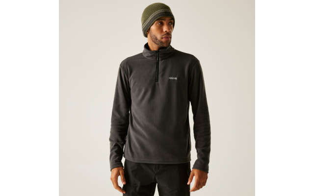Personne portant une polaire gris foncé à demi-fermeture éclair, un bonnet tricoté vert olive et un pantalon noir sur fond clair