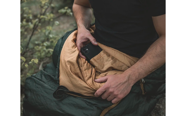 Een persoon zit buiten met een telefoon in de hand op een rugzak