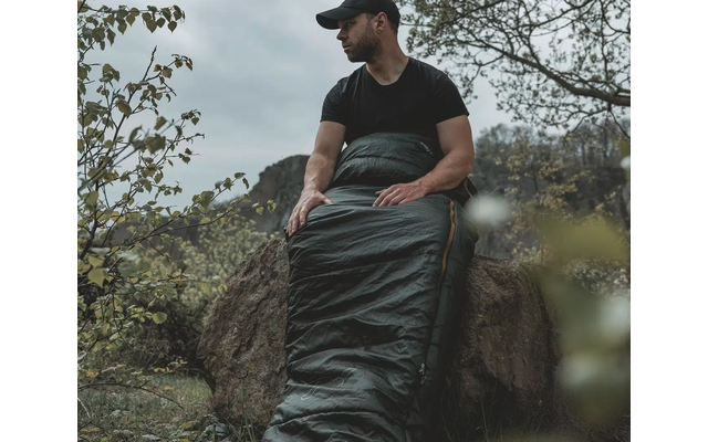 Een man met een zwart t-shirt en honkbalpet zit op een boomstam, omgeven door bomen
