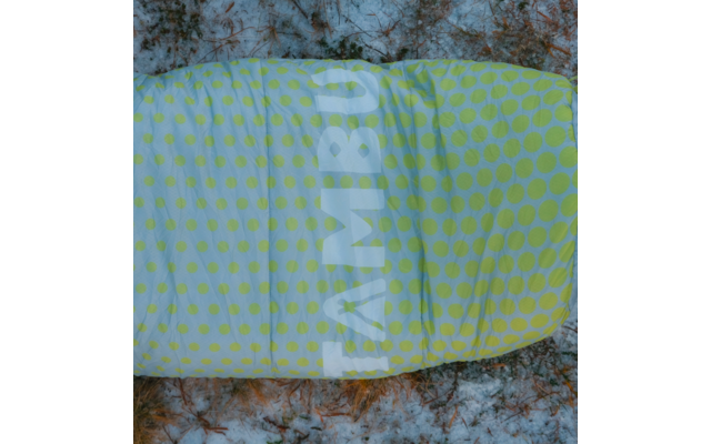 Yellow-green sleeping bag with light-green polka dots and vertical white lettering on snowy, partly grassy ground