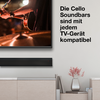 TV mit Nahaufnahme einer Gitarre und Händen, darunter schwarze Soundbar, niedriges Sideboard mit Vase und rosa Blumen; rechter Wandtext: Die Cello Soundbars sind mit jedem TV-Gerät kompatibel