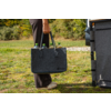 Hand einer Person hält eine graue Filztasche mit mehreren Flaschen mit grünen Verschlüssen; Beine und Schuhe sichtbar, Person steht auf Gras neben einem Fahrzeug