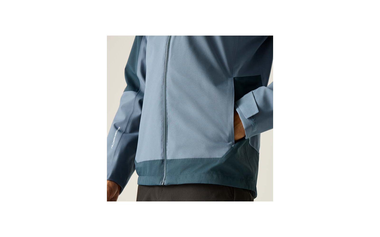 Oberkörper in hellblauer Jacke mit Reißverschluss, Hand in Seitentasche, dunkler Saum, sichtbares Handgelenk