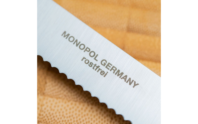 Gros plan d'une lame de couteau dentelée avec l'inscription 'MONOPOL GERMANY rostfrei' sur un fond brun texturé