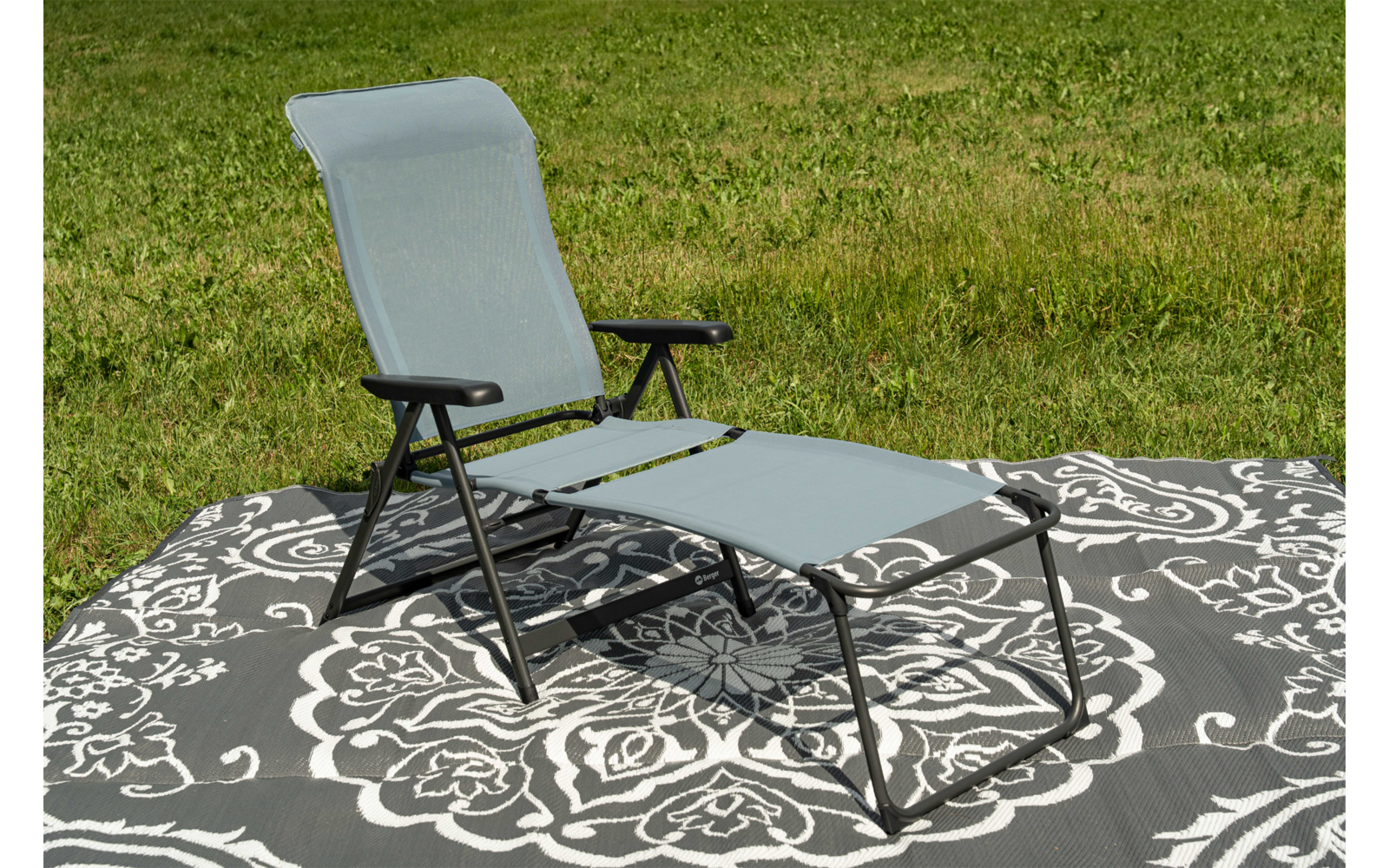 Outdoor-Liegestuhl mit schwarzem Metallgestell und hellblauer Sitz- und Rückenbespannung, ausgezogene Fußstütze, auf einem grauen Teppich mit weißem Blumenmuster auf Gras