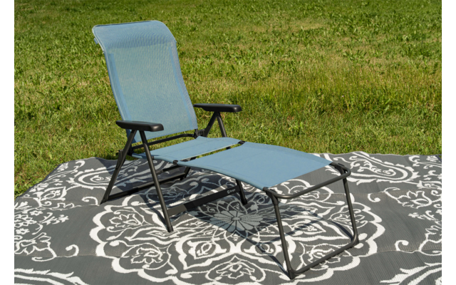 Silla reclinable azul sobre manta gris con estampado blanco sobre césped