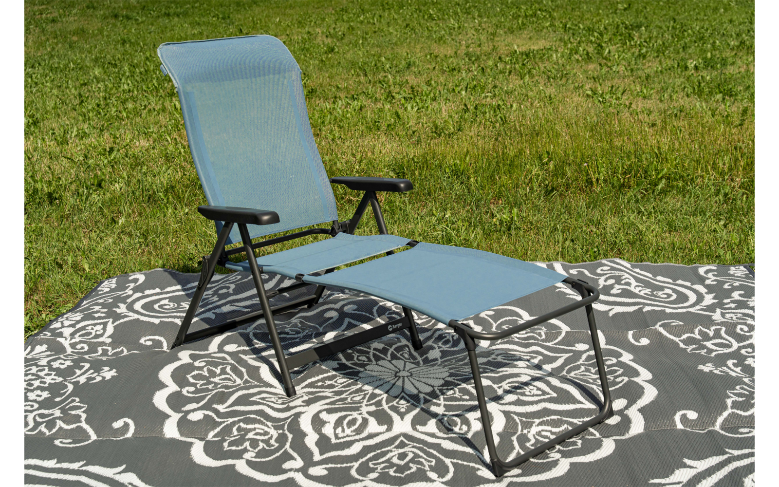 Silla reclinable azul sobre manta gris con estampado blanco sobre césped