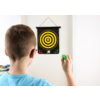 Ein Junge von hinten hält einen Dartpfeil und zielt auf eine Dartscheibe an der Wand