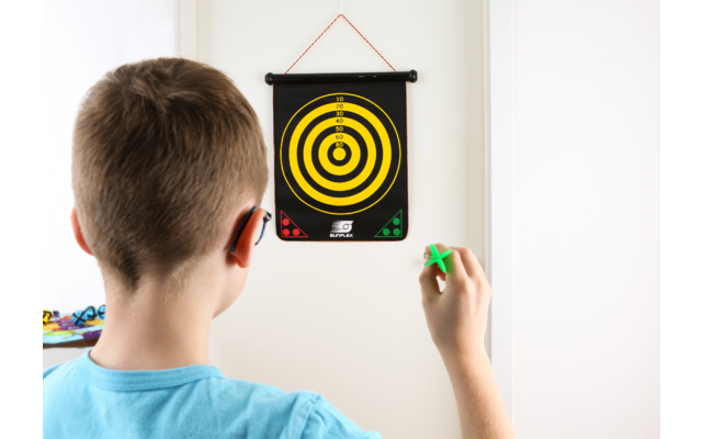 Ein Junge von hinten hält einen Dartpfeil und zielt auf eine Dartscheibe an der Wand