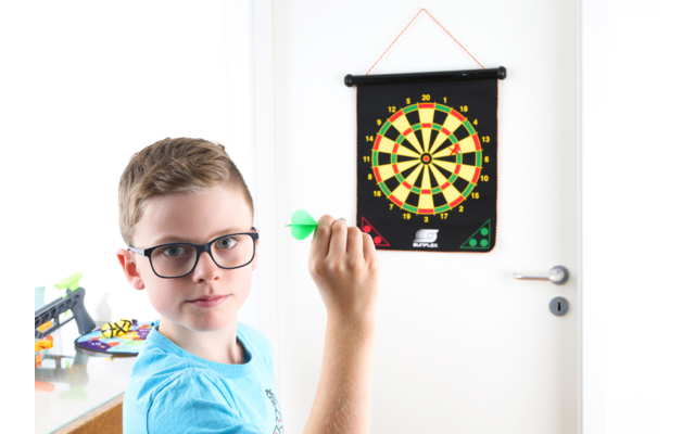 Junge mit Brille wirft Dartpfeil auf eine Dartscheibe an der Wand