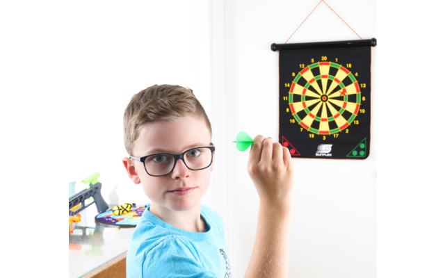 Garçon avec des lunettes lance une fléchette sur une cible accrochée au mur