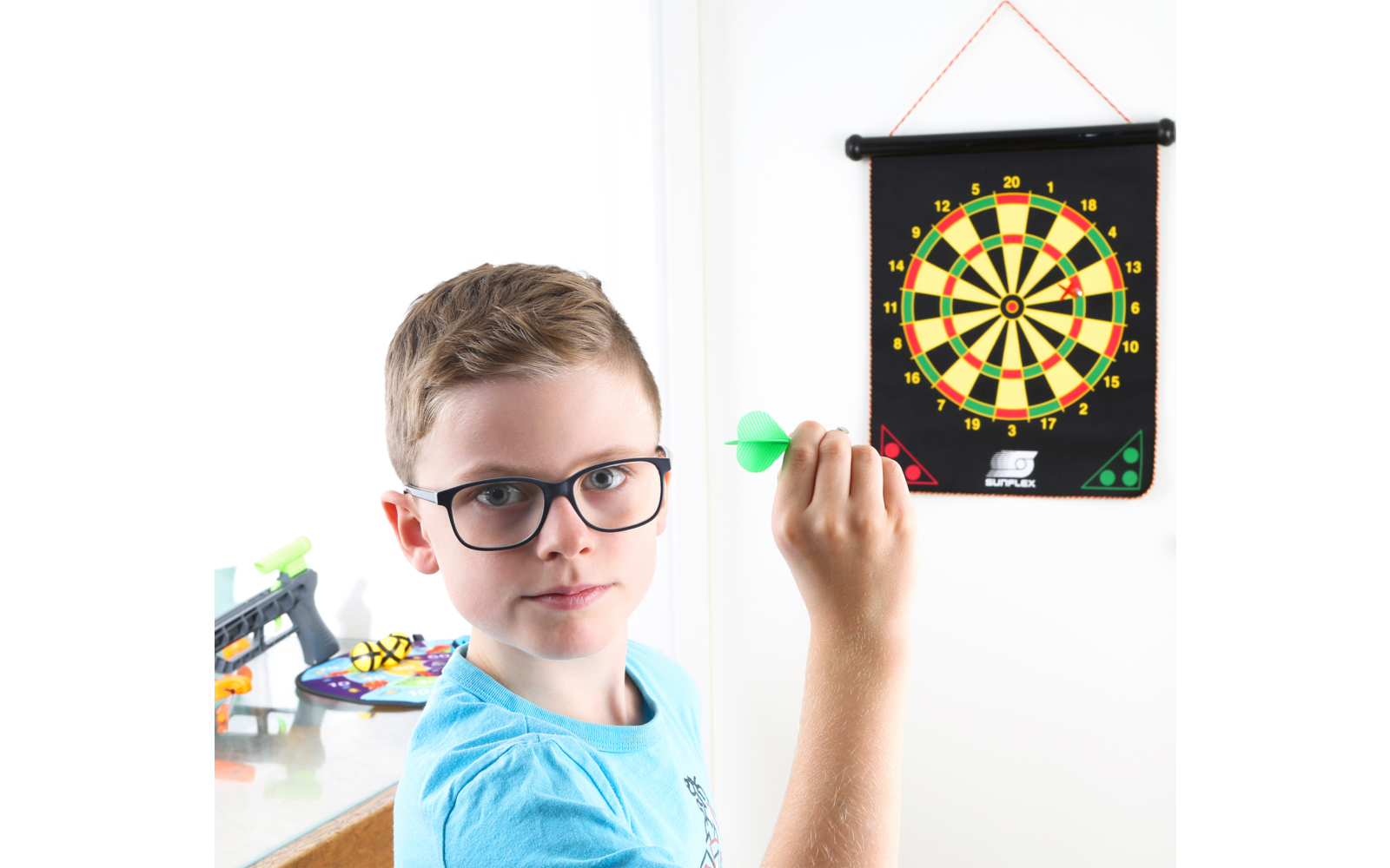 Garçon avec des lunettes lance une fléchette sur une cible accrochée au mur