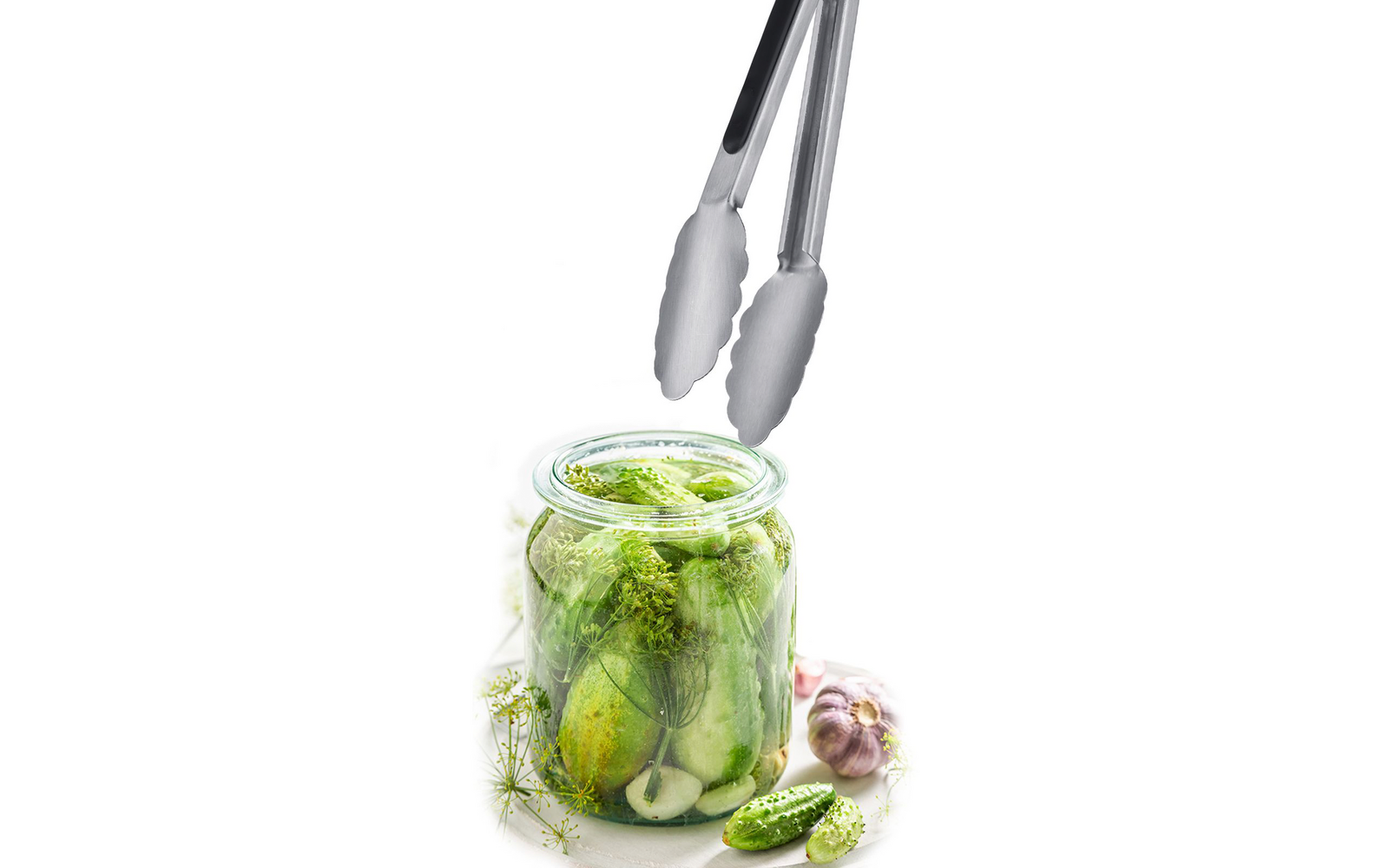 Glas mit kleinen ganzen und geschnittenen Gurken, Dill und Knoblauch, Metallzange über dem Glas