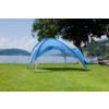 Blauer Pavillon auf grünem Rasen am Seeufer; im Hintergrund See, Boote, Personen am Steg, Bäume und Hügel unter leicht bewölktem Himmel