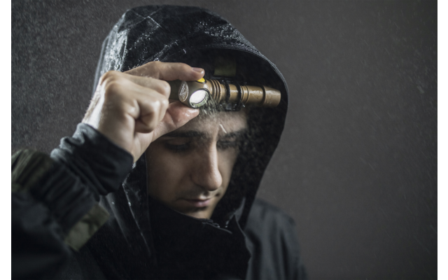 Person mit Kapuzenpullover hält eine Taschenlampe neben das Auge