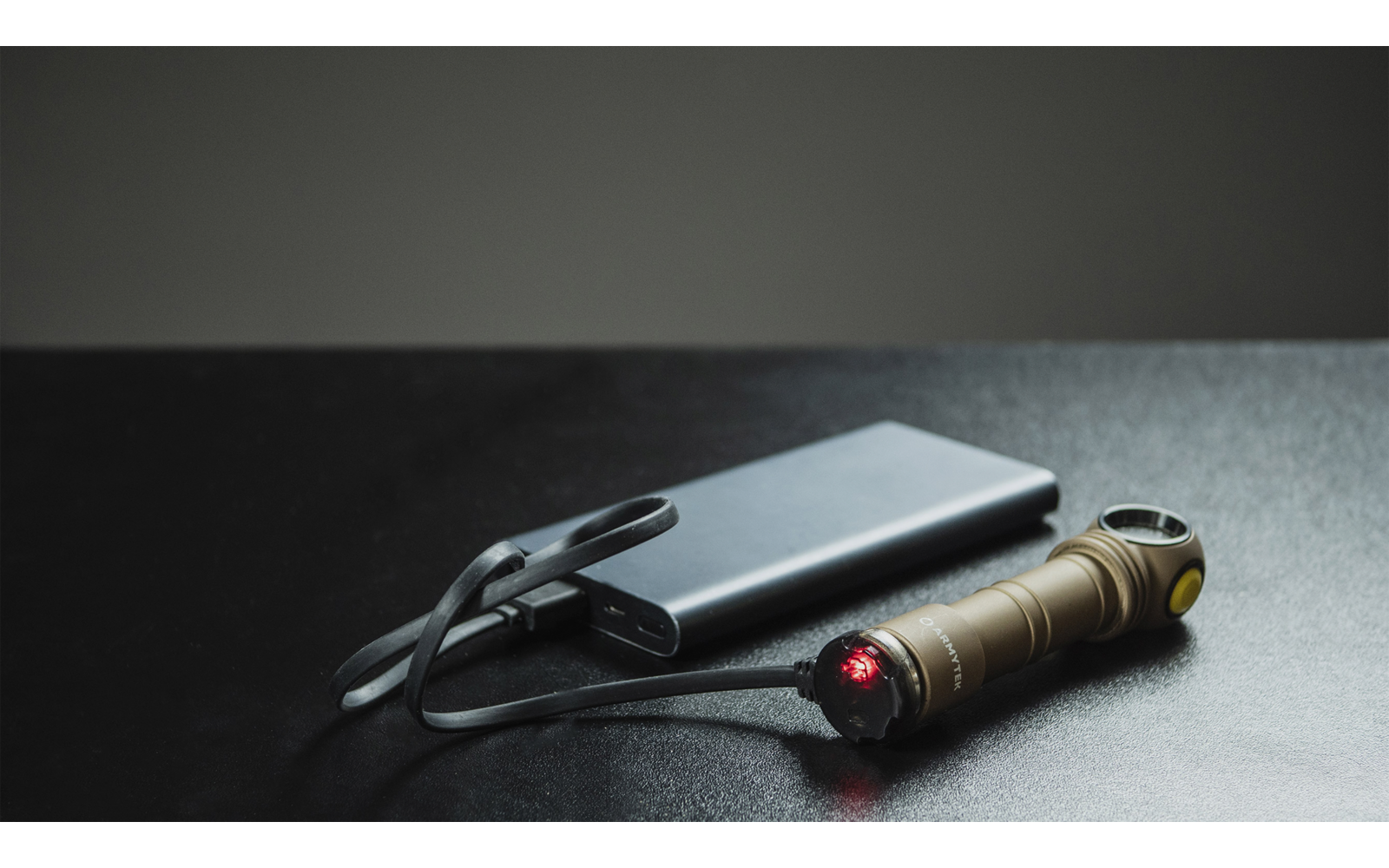 Eine goldene Taschenlampe liegt auf einer schwarzen Oberfläche neben einer Powerbank mit daran angeschlossenem Ladekabel