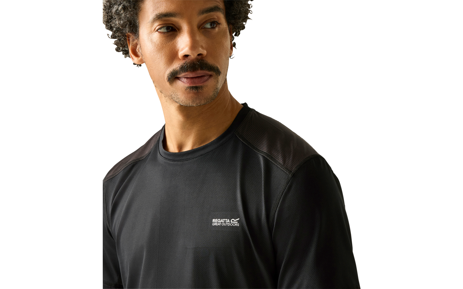 Porträt einer Person von Brusthöhe, mit kurzem lockigem Haar und Schnurrbart, blickt nach links, trägt ein schwarzes Langarm-Sportshirt mit kleinem weißen Logo auf der linken Brust