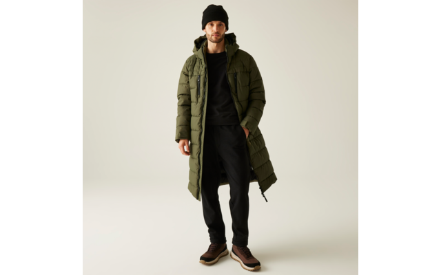 Ein Mann trägt einen langen olivgrünen Mantel, schwarzen Pullover, schwarze Hose und braune Schuhe