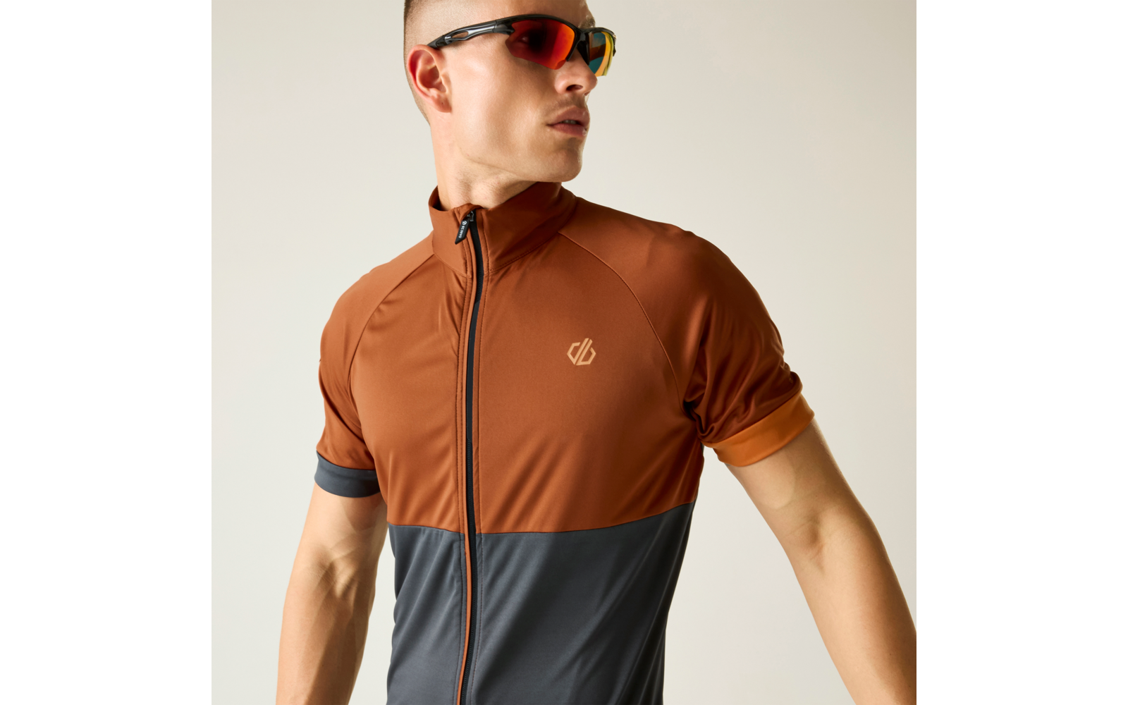 Persona con prenda superior marrón de manga corta con cremallera frontal y parte inferior gris oscuro, lleva gafas de sol, mira hacia la izquierda