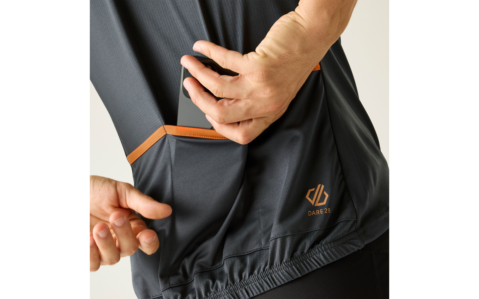 Dos manos sujetando un bolsillo lateral de una camiseta deportiva gris oscuro con ribete naranja y pequeño logotipo naranja
