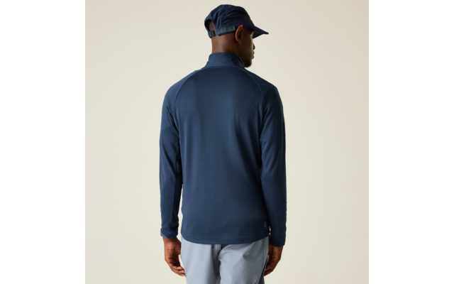 Person von hinten, trägt dunkelblaues langärmeliges Oberteil mit Stehkragen, dunkelblaue Kappe und hellgraue Hose vor beigem Hintergrund