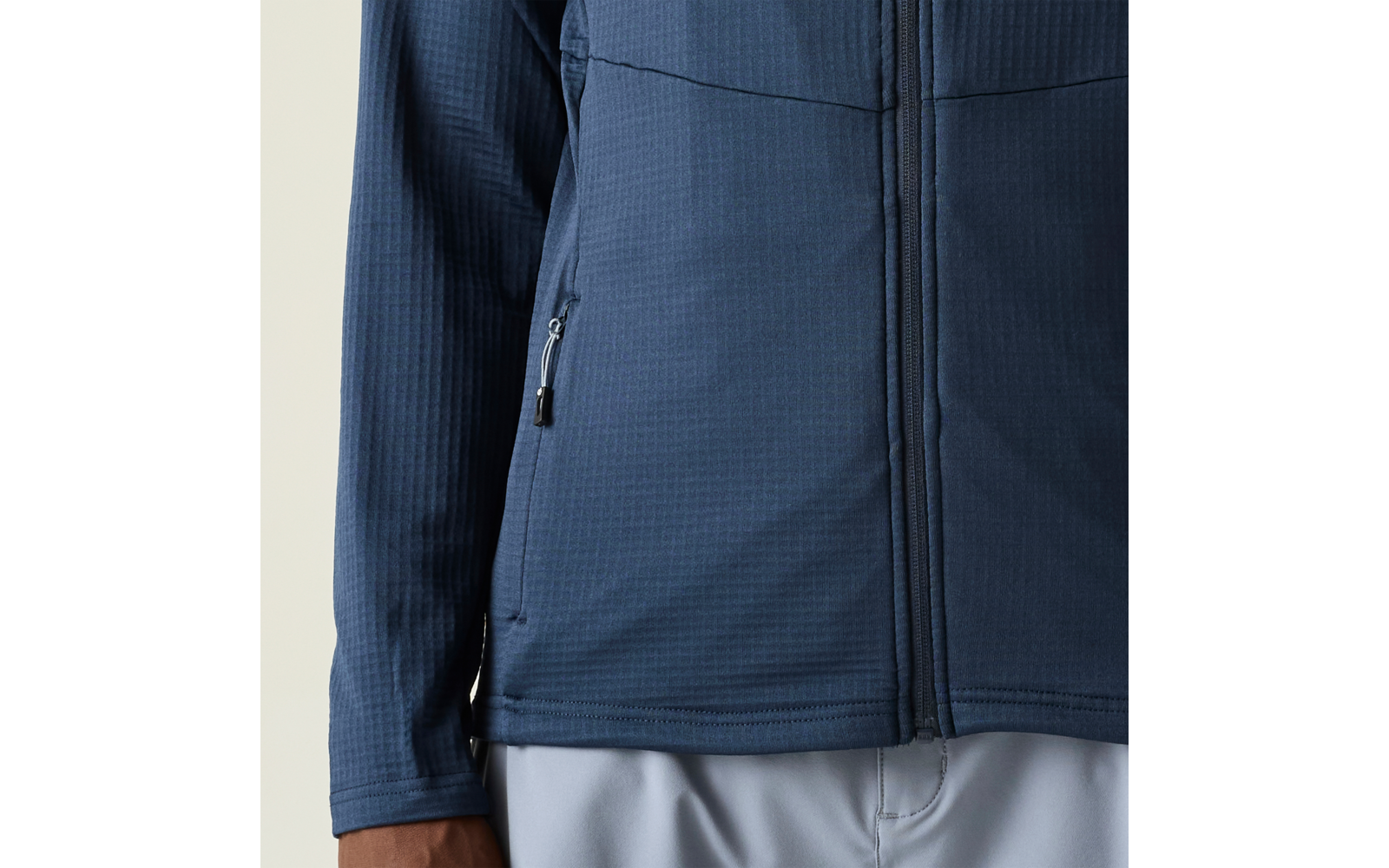 Dunkelblaue Jacke mit durchgehendem Reißverschluss und seitlicher Reißverschlusstasche, langes Ärmelende, teilweise sichtbare Hand, hellgraue Hose