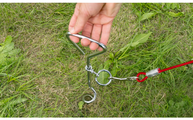 Hand hält einen Metallgriff, der an einer Spiralfeder befestigt ist, auf Grasboden
