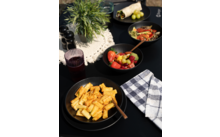 Teller mit Pasta, daneben eine Serviette und ein Glas Rotwein auf einem Holztisch, im Hintergrund Kräuter und Knoblauch