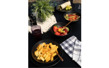 Teller mit Pasta, daneben eine Serviette und ein Glas Rotwein auf einem Holztisch, im Hintergrund Kräuter und Knoblauch