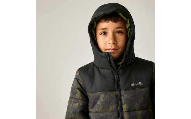 Kind mit dunklen Haaren und Sommersprossen, Kapuze hoch, dunkle gesteppte Jacke mit Reißverschluss und Logo vor hellem Hintergrund