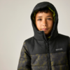 Kind mit dunklen Haaren und Sommersprossen, Kapuze hoch, dunkle gesteppte Jacke mit Reißverschluss und Logo vor hellem Hintergrund
