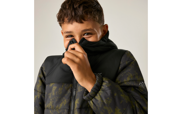 Junge zieht den Kragen seiner gepolsterten Jacke vor den Mund, blickt in die Kamera, einfarbiger heller Hintergrund