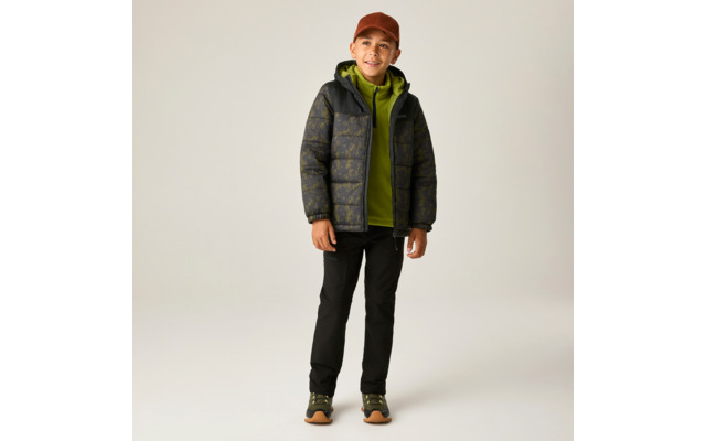 Junge steht, trägt braune Kappe, grüne Kapuzenjacke unter dunkel gemusterter Steppjacke, schwarze Hose und grün-braune Sneakers vor hellem Hintergrund