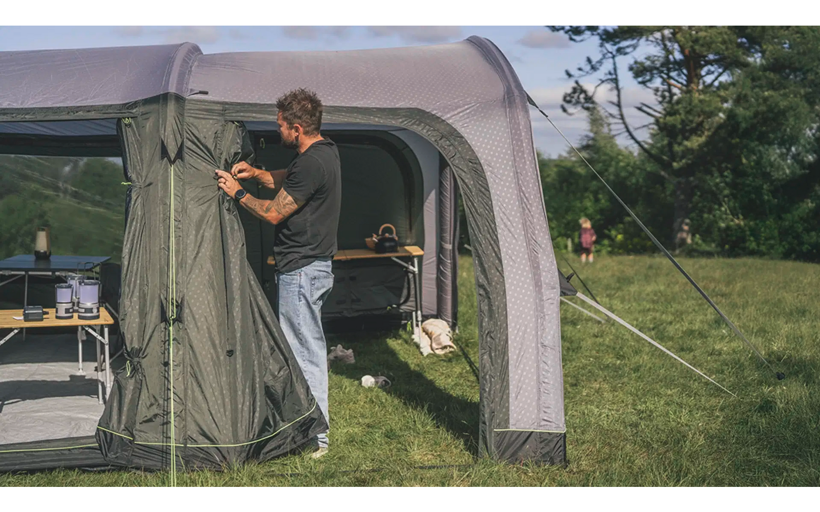 Mann öffnet einen Zeltvorbau im Freien bei Sonnenschein