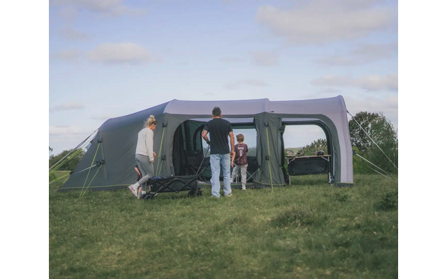 Zwei Personen stehen vor einem großen, grauen Zelt auf einem Campingplatz unter einem bewölkten Himmel