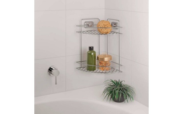 Étagère d'angle métallique sur mur carrelé de la salle de bain au-dessus de la baignoire ; étagère supérieure avec éponge ronde et objet plat, étagère inférieure avec bouteille verte et récipient transparent contenant des billes orange ; sur le bord de la baignoire un pot noir avec plante verte ; poignée de robinet chromée à gauche