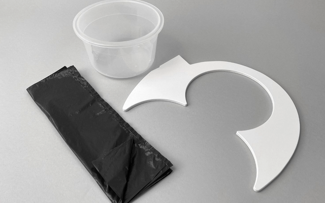 Un gobelet en plastique transparent, un sac-poubelle noir roulé et une pièce en plastique blanche en forme de demi-cercle sur une surface grise