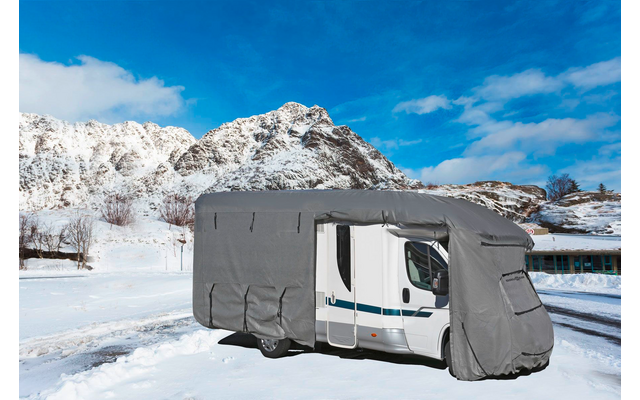 Ein Wohnmobil mit grauer Abdeckung auf schneebedecktem Boden vor schneebedeckten Bergen und blauem Himmel