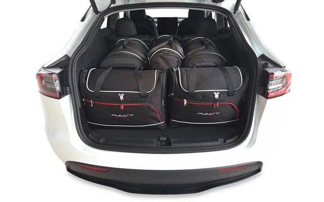 Coffre ouvert d'une voiture blanche avec cinq sacs de voyage noirs à liseré rouge, deux à l'avant et trois à l'arrière, sièges arrière visibles